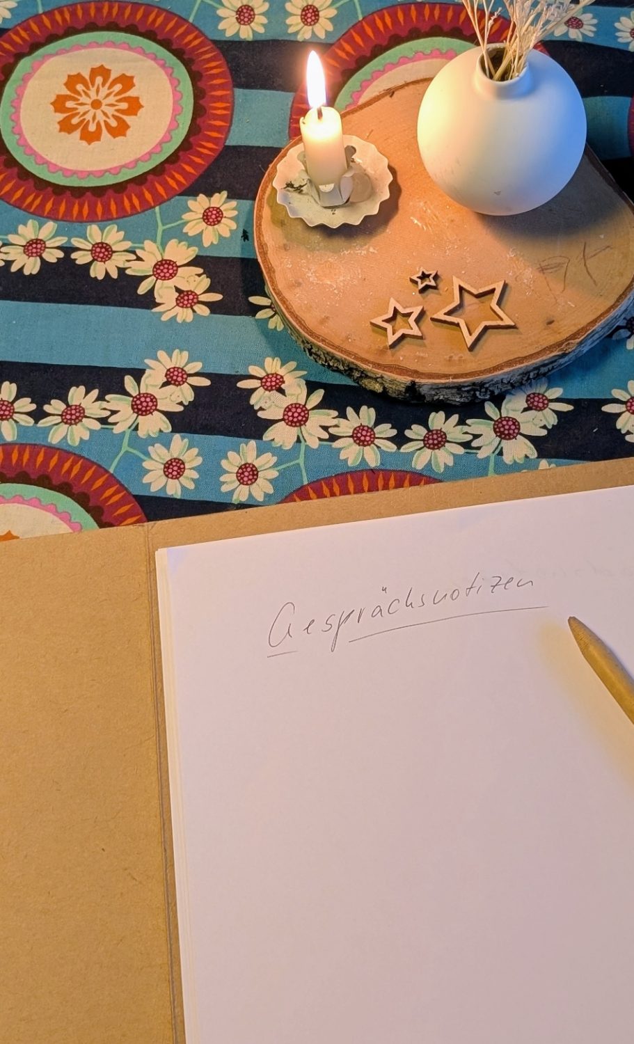 Ein aufgeschlagenes Notizbuch mit der Überschrift Gesprächsnotizen, ein Stift und eine brennende Kerze