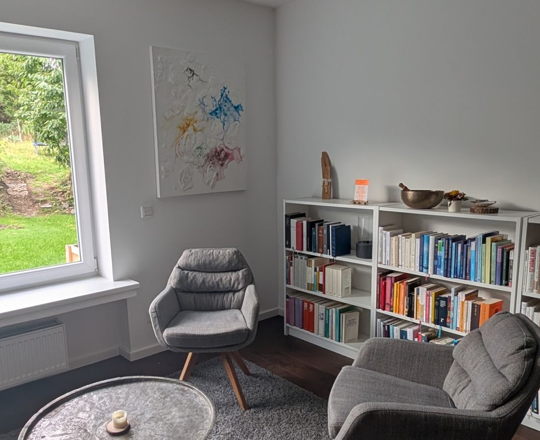 Der Beratungsraum in Wuppertal: zwei Sessel, ein runder Tisch mit Kerze, Bücherregale und ein Fenster ins Grüne